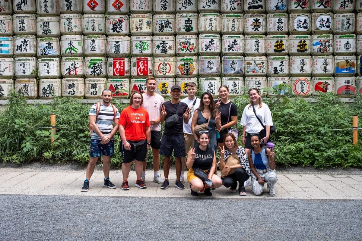 A tour group posing in front of a wall of painted sake barrels at a Tokyo shrine