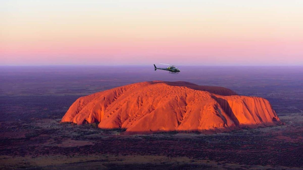 Uluru glowing orange at sunrise over the desert scrub