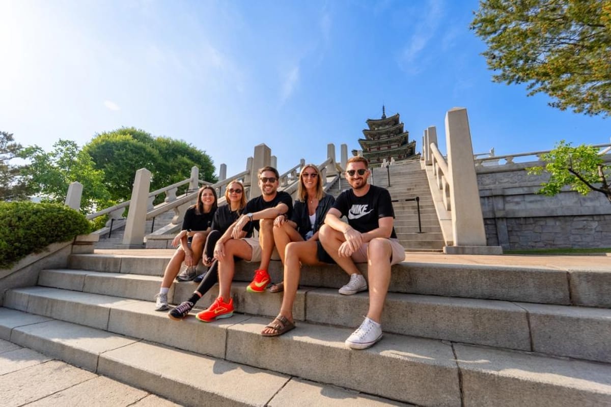 Five young travellers sitting on stone steps at Gyeongbokgung Palace in Seoul on a sunny day, with a tiered pagoda behind them