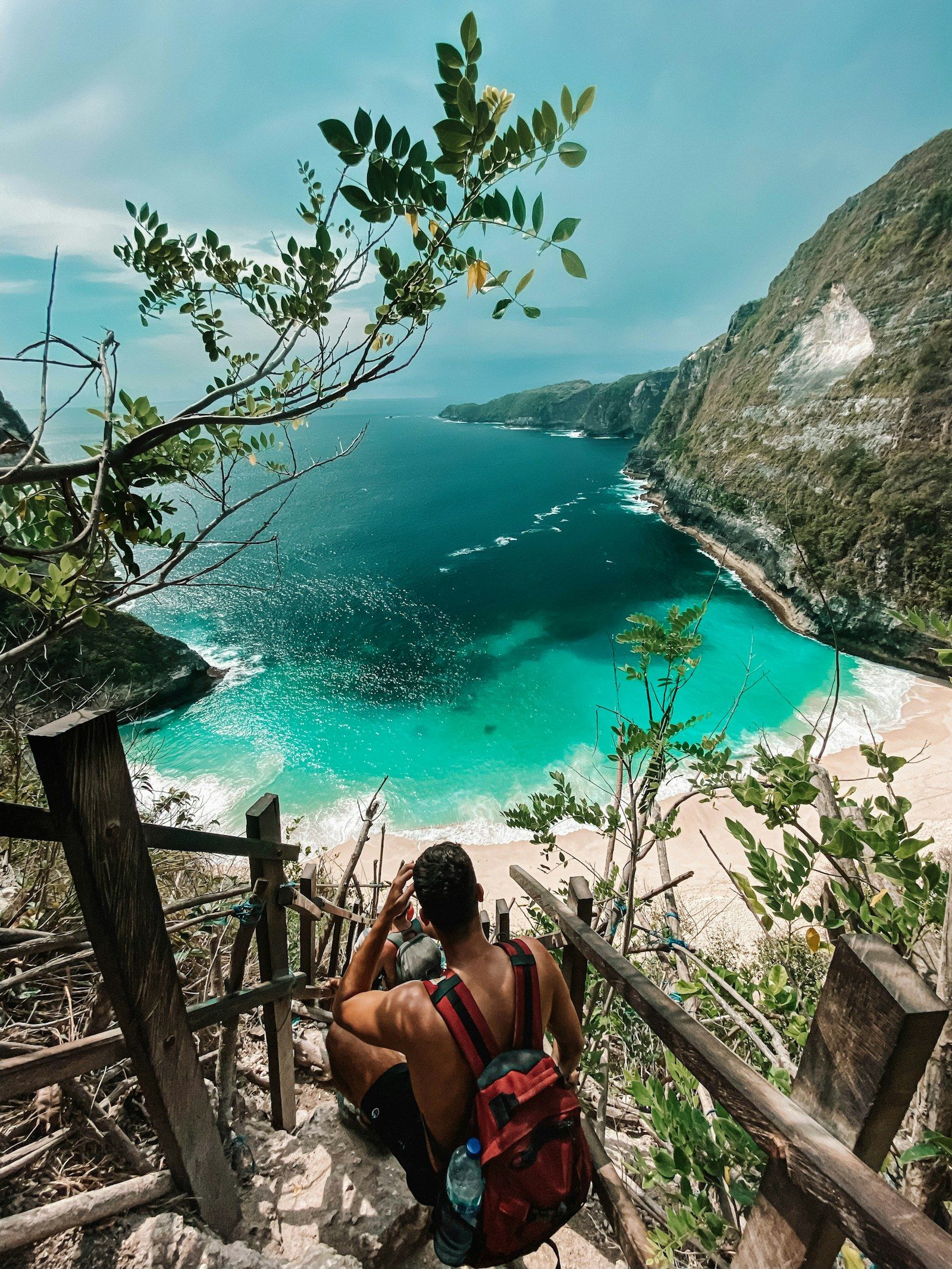 A traveller on the cliff steps above a turquoise cove on Nusa Penida, Bali