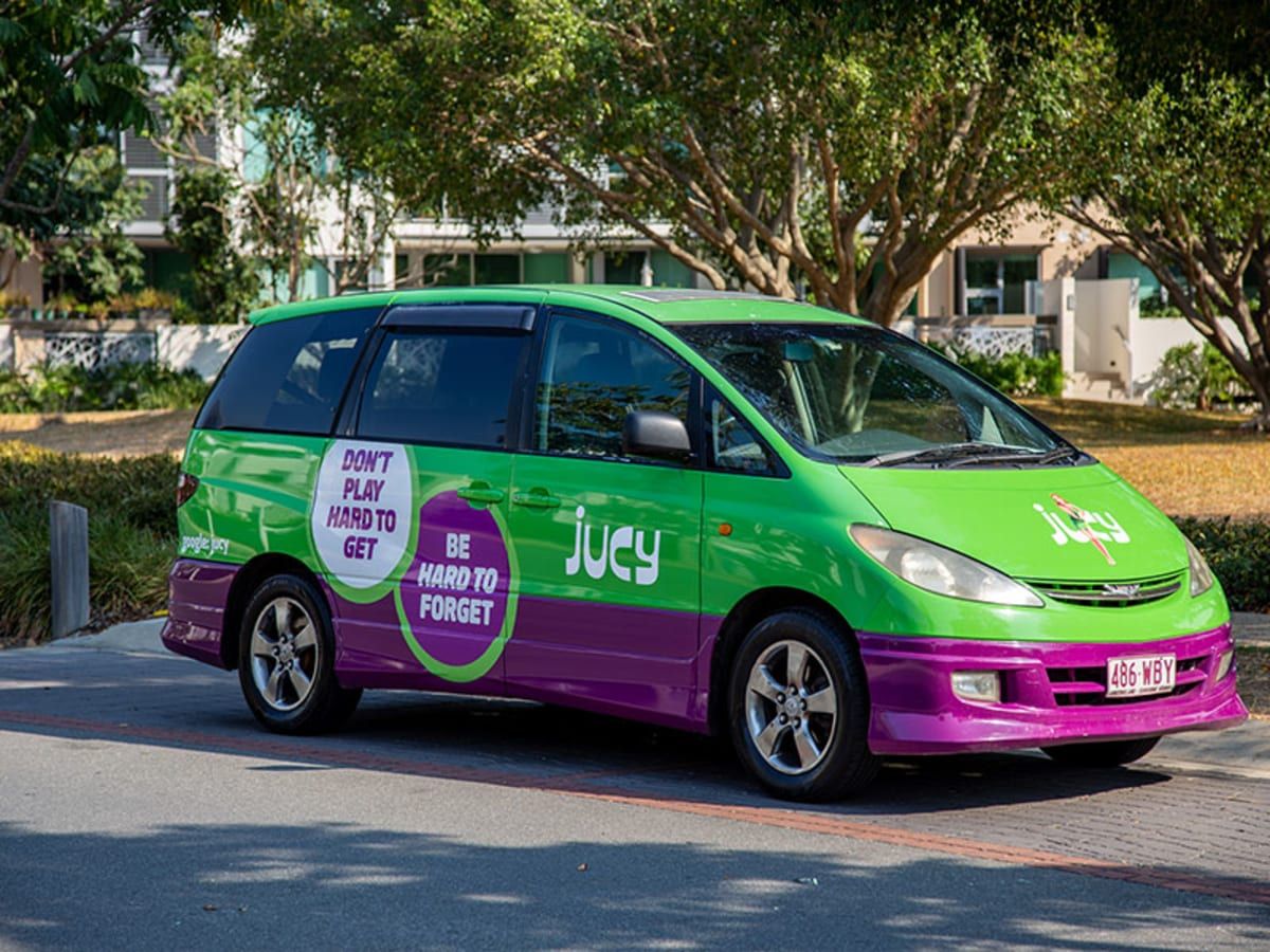 A green and purple 2-berth people-mover campervan parked under trees