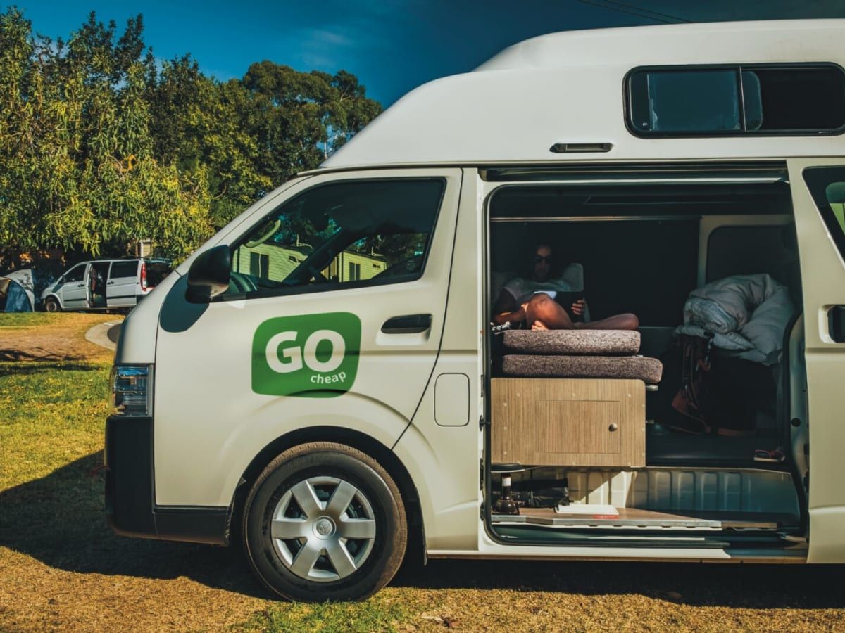 A white hi-top campervan with its side door open, parked at a campground