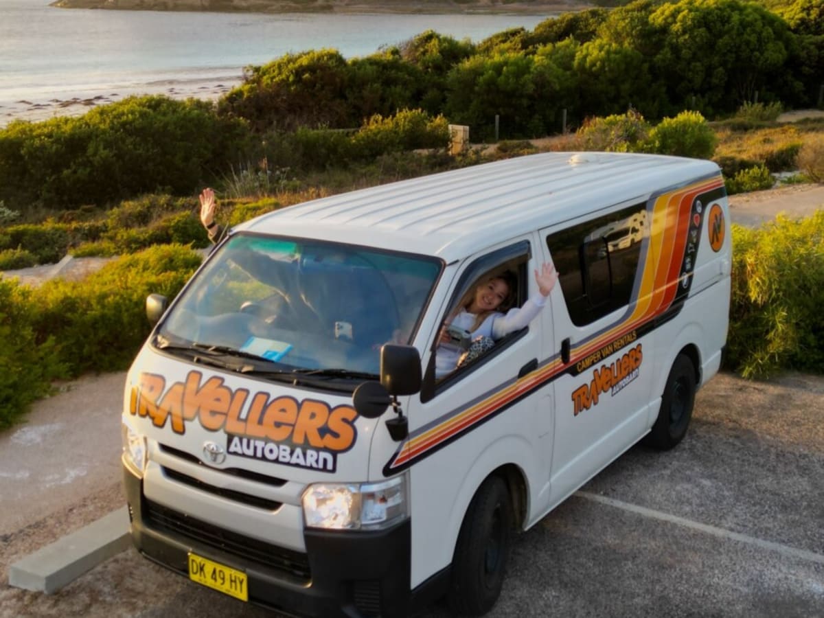 A white campervan with an orange stripe parked beside a bay