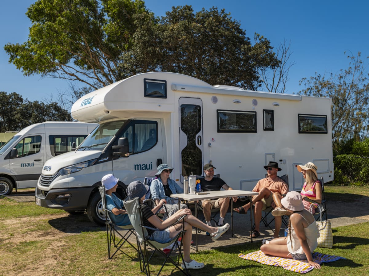 A white motorhome parked on grass at a caravan park with a group sitting outside