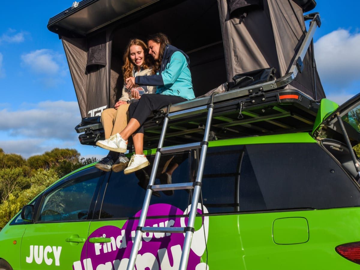 Two travellers sitting in the rooftop tent of a green campervan