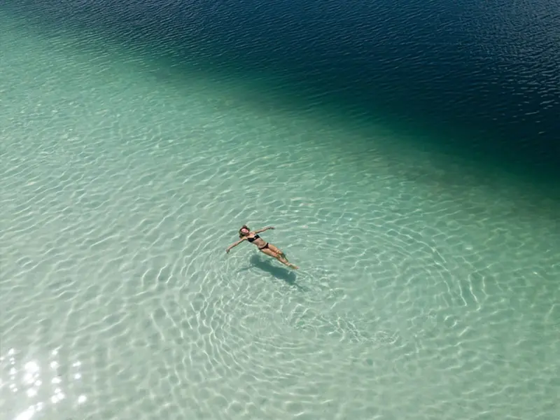 A traveller floating alone in the clear water of Lake McKenzie on K'gari
