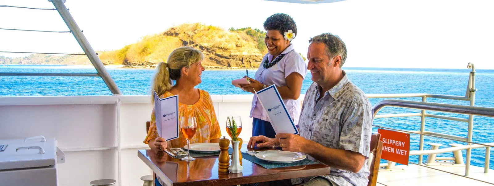 Guests seated at a table on the open deck, ordering from a crew member